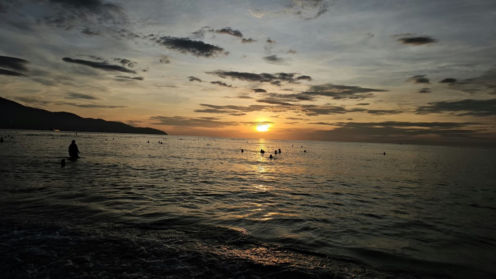 Sunset over the sea at a beach, with swimmers in silhouette