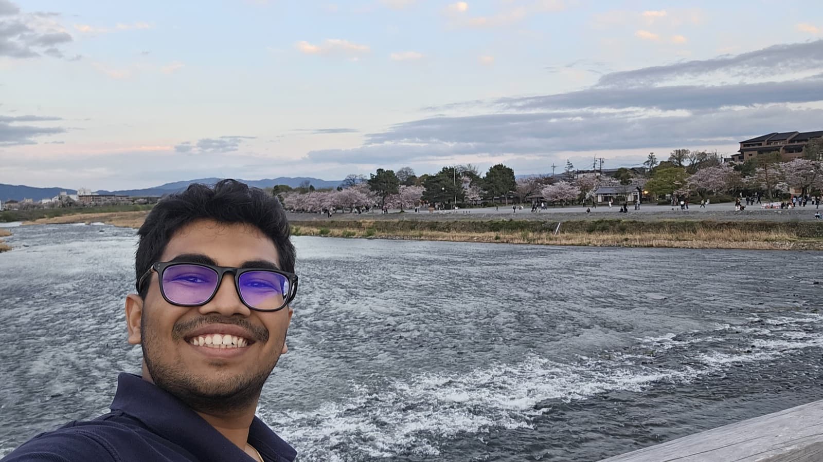 Ishan smiling in front of a river in Kyoto at dusk