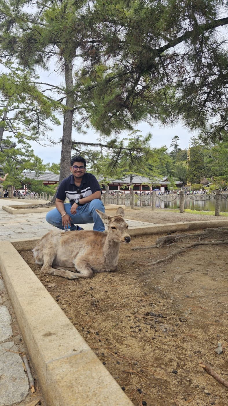 Ishan crouching next to a resting deer in Nara park