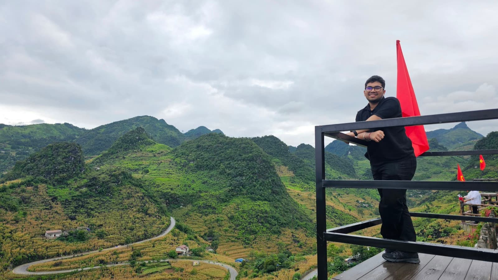 Ishan on a viewing platform above green karst mountains and a winding road